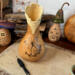 This shows a gourd with a butterfly wood burned onto the front. The top is carved into a wavy rim. Mushroom gourds sit in the background. 